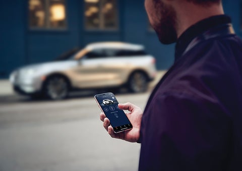 A person is shown interacting with a smartphone to connect to a Lincoln vehicle across the street. | Dorsch Lincoln in Green Bay WI