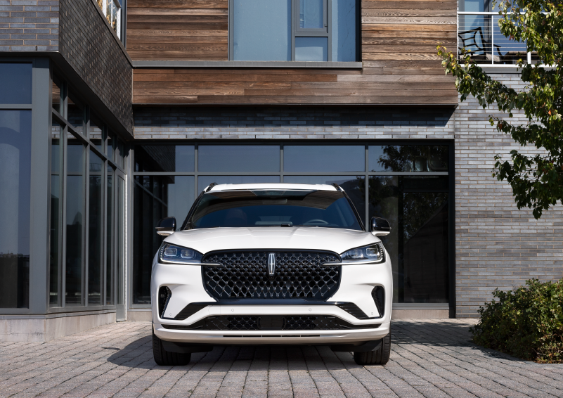 A white 2025 Lincoln Aviator® SUV is shown parked outside a modern building with gray brick and wood accents. | Dorsch Lincoln in Green Bay WI