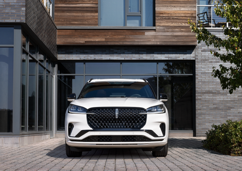 A white 2025 Lincoln Aviator® SUV is shown parked outside a modern building with gray brick and wood accents. | Dorsch Lincoln in Green Bay WI