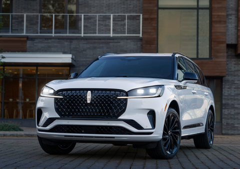 A white 2025 Lincoln Aviator® SUV is shown parked outside a modern building with gray brick and wood accents. | Dorsch Lincoln in Green Bay WI