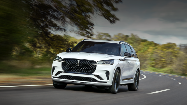 A white 2025 Lincoln Aviator® SUV is being driven down a road lined with trees. | Dorsch Lincoln in Green Bay WI