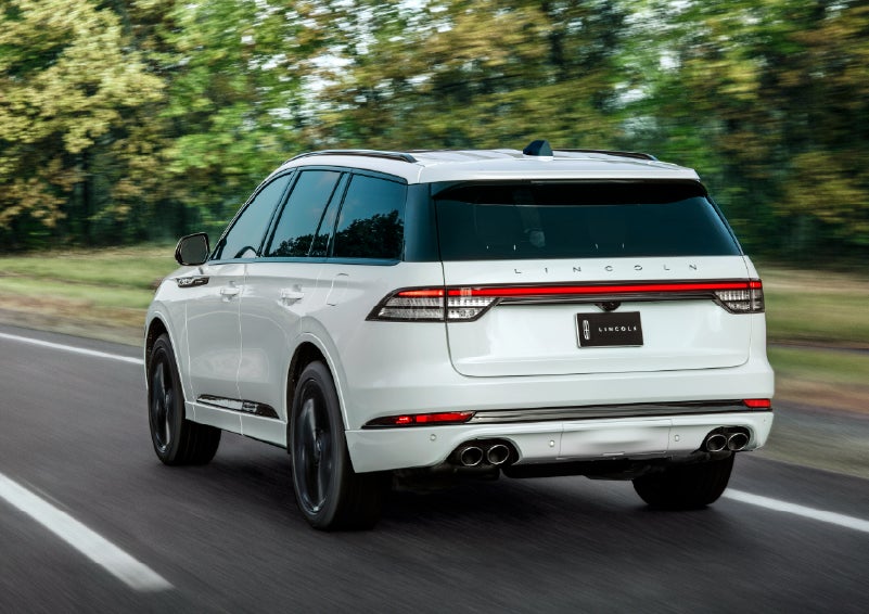 A white 2026 Lincoln Aviator® SUV is being driven away down a road lined with colorful trees. | Dorsch Lincoln in Green Bay WI
