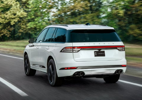 A white 2026 Lincoln Aviator® SUV is being driven away down a road lined with colorful trees. | Dorsch Lincoln in Green Bay WI