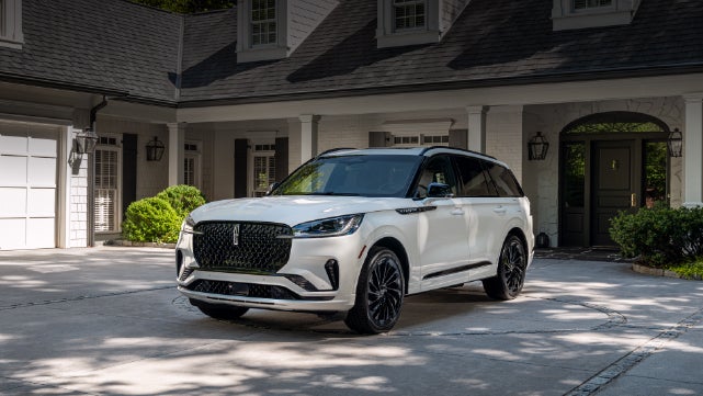 A white 2026 Lincoln Aviator® SUV is parked in the driveway of a luxury home. | Dorsch Lincoln in Green Bay WI