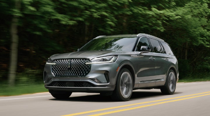 A 2027 Lincoln Aviator® SUV is being driven down a road lined with trees. | Dorsch Lincoln in Green Bay WI