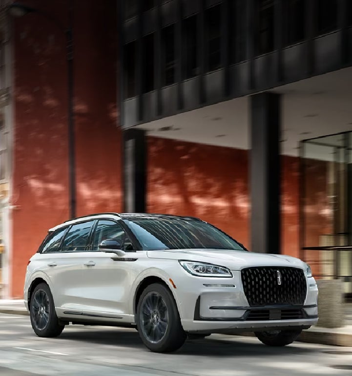 The 2024 Lincoln Corsair® SUV with the Jet Appearance Package and a Pristine White exterior is being driven down a city street.